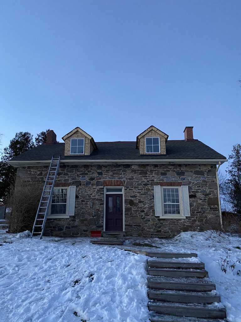 A house with snow on the ground and a ladder in front of it.
