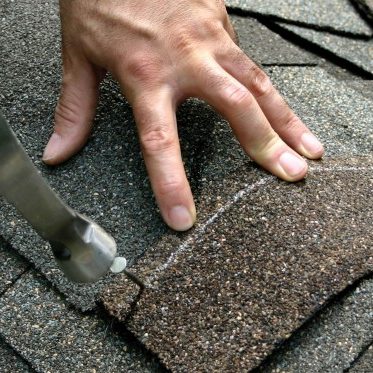 A person is cutting the shingles off of a roof.