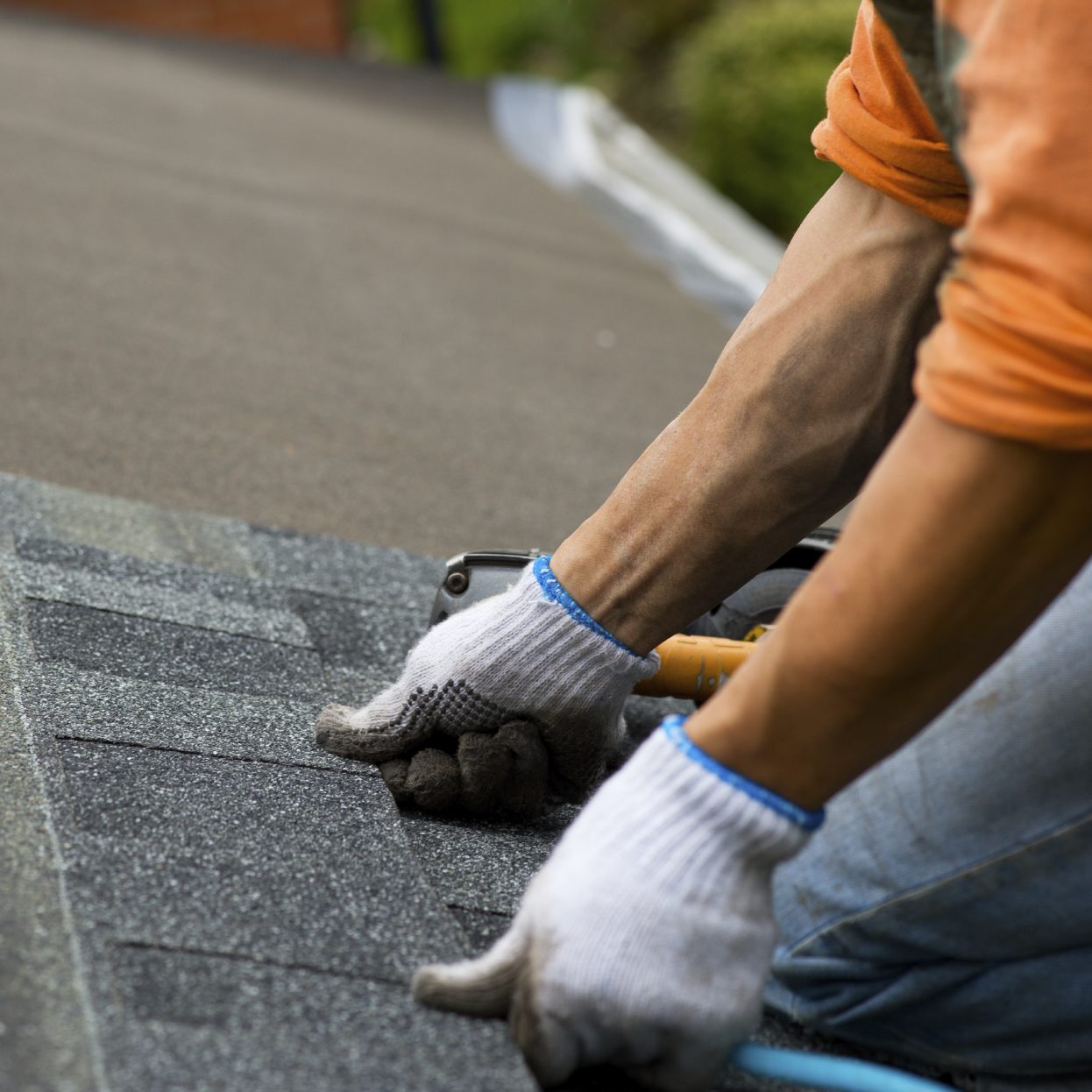 A person with gloves on working on the roof of a house.